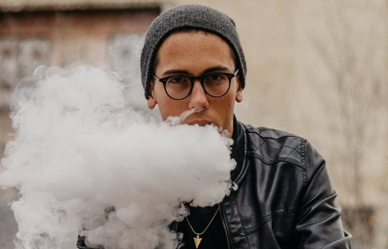 Un garçon qui fume et émet un gros nuage de vapeur.