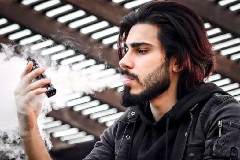 Garçon regardant l'e-cig qu'il tient en fumant une cigarette. | Terpy